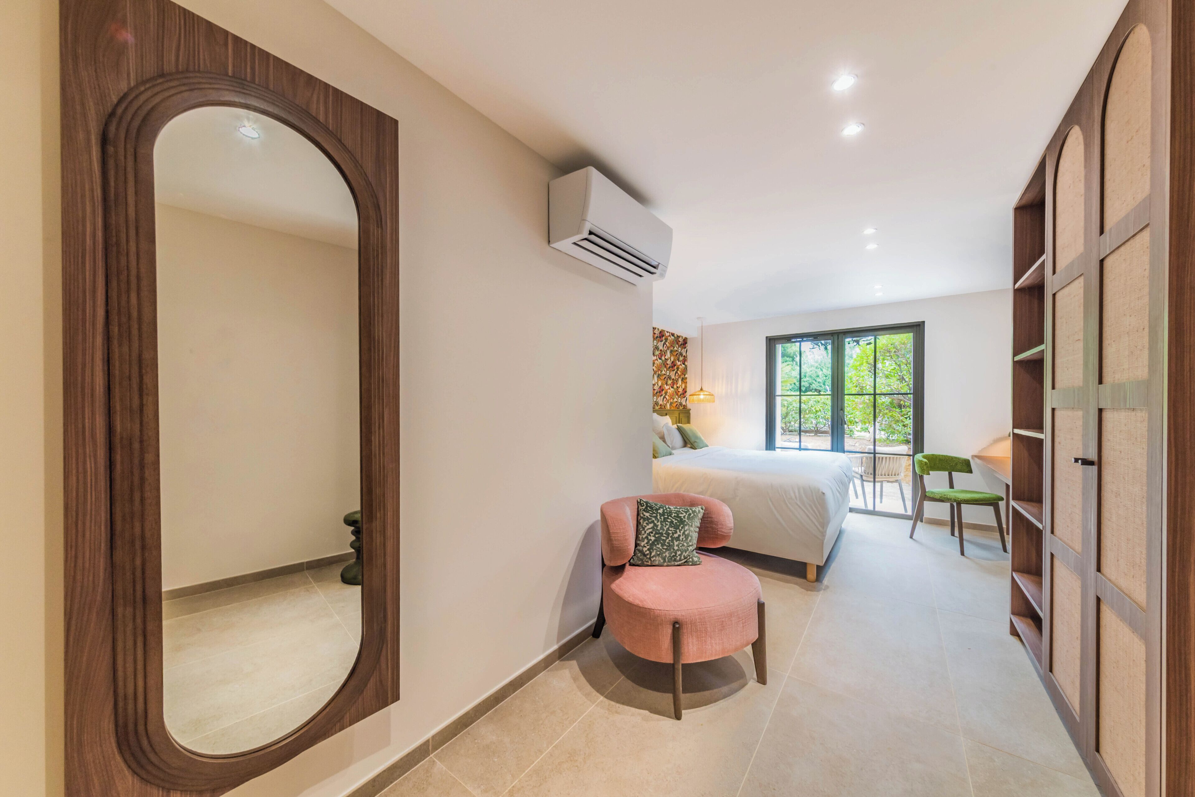 A bedroom with a large mirror, a bed, a chair, a desk, and a wardrobe.