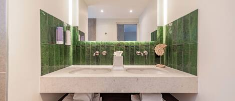 A bathroom with a double sink, green tiles, a mirror, and a wooden vanity.