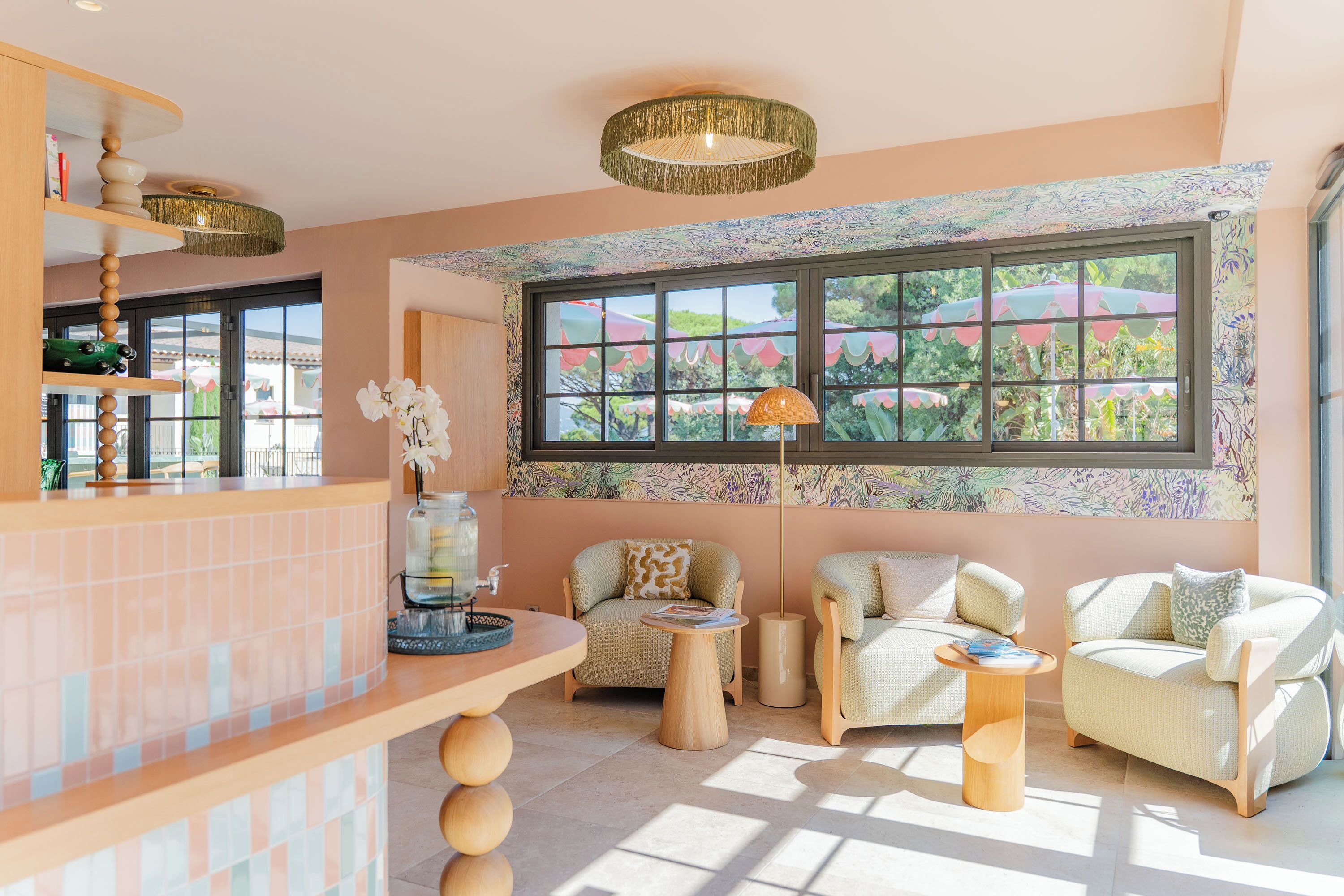 Una habitación luminosa con un ventanal grande, dos sillones, una mesita y una zona de bar con una lámpara decorativa.
