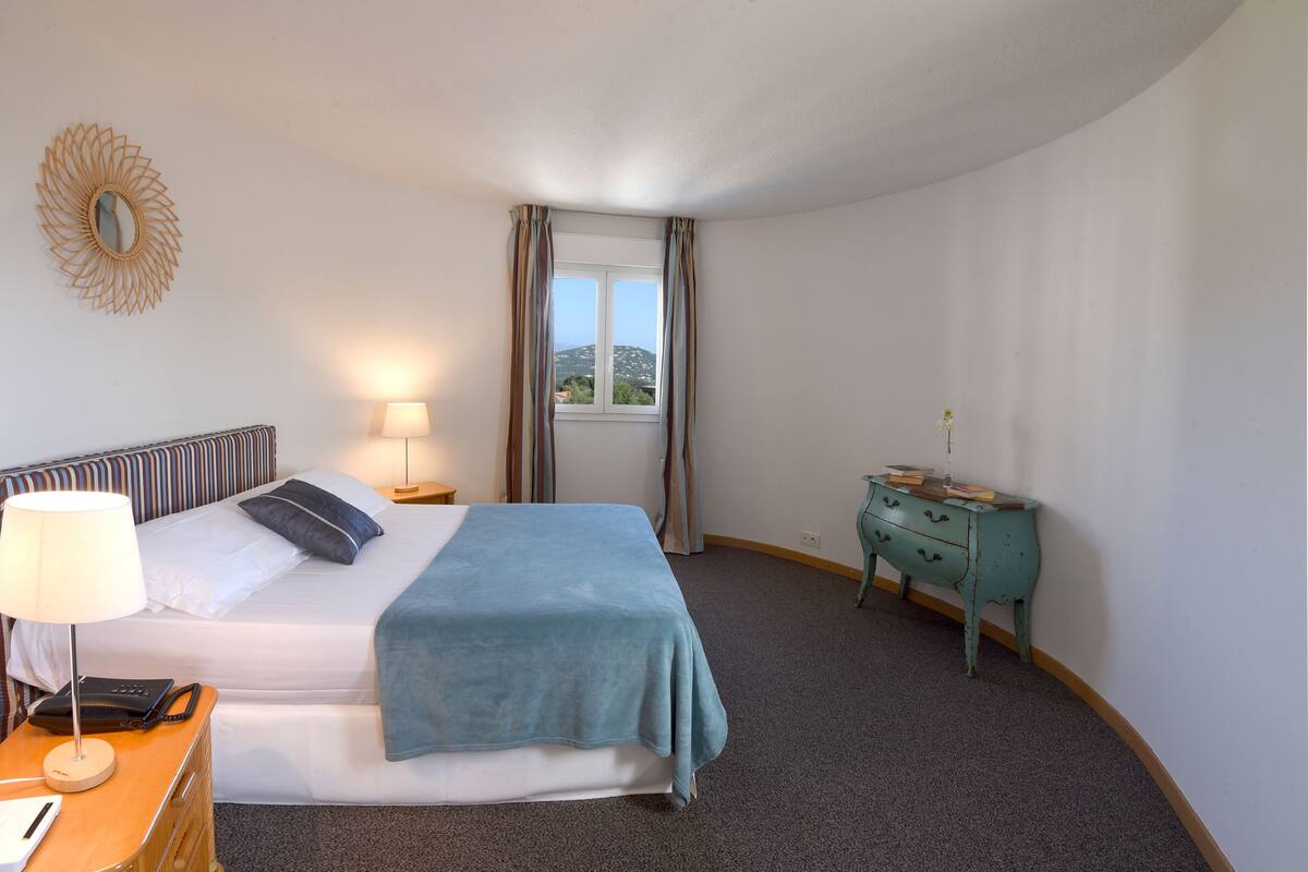 Habitación de hotel con cama, lámpara de noche, teléfono y cómoda.