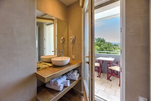A bathroom with two sinks, a large mirror, and a view of an outdoor patio with red chairs and a table. - Hotel Le Tilbury (Porto-Vecchio)