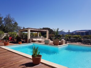 A pool area with a wooden deck, lounge chairs, and a covered seating area. - Hotel Le Tilbury (Porto-Vecchio)