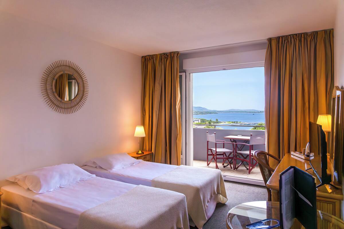 Habitación de hotel con dos camas, un escritorio, una silla, un televisor y un balcón con vista al mar.