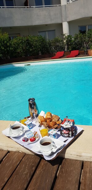 A breakfast setup by a pool with croissants, pastries, coffee, and juice. - Hotel Le Tilbury (Porto-Vecchio)