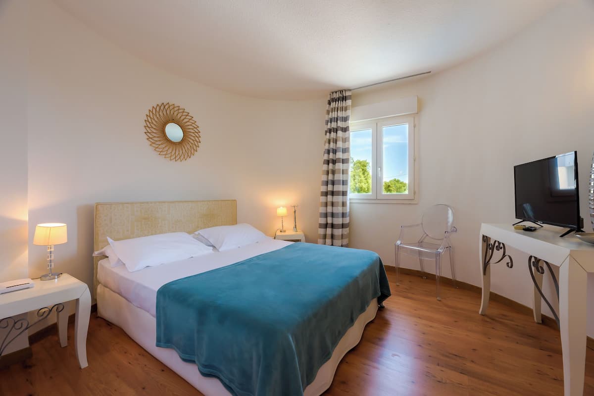 Un dormitorio con cama, mesitas de noche, televisión y ventana con cortinas.