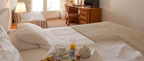 A hotel room with two beds, a desk with a TV, and a breakfast tray with croissants, juice, and coffee.