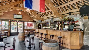 A bar area with wooden stools, a bar counter, and a stone wall. - Domaine Des Ormes (Epiniac)