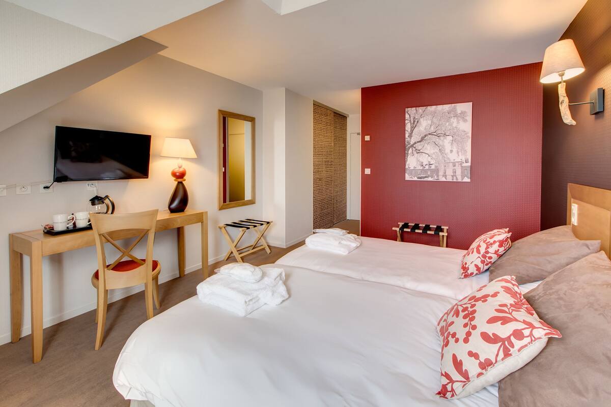 A hotel room with two beds, a desk, a chair, a TV, and a red accent wall.