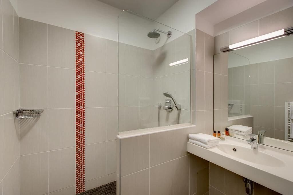 A modern bathroom with a glass shower enclosure, a large mirror, and a sink with toiletries.