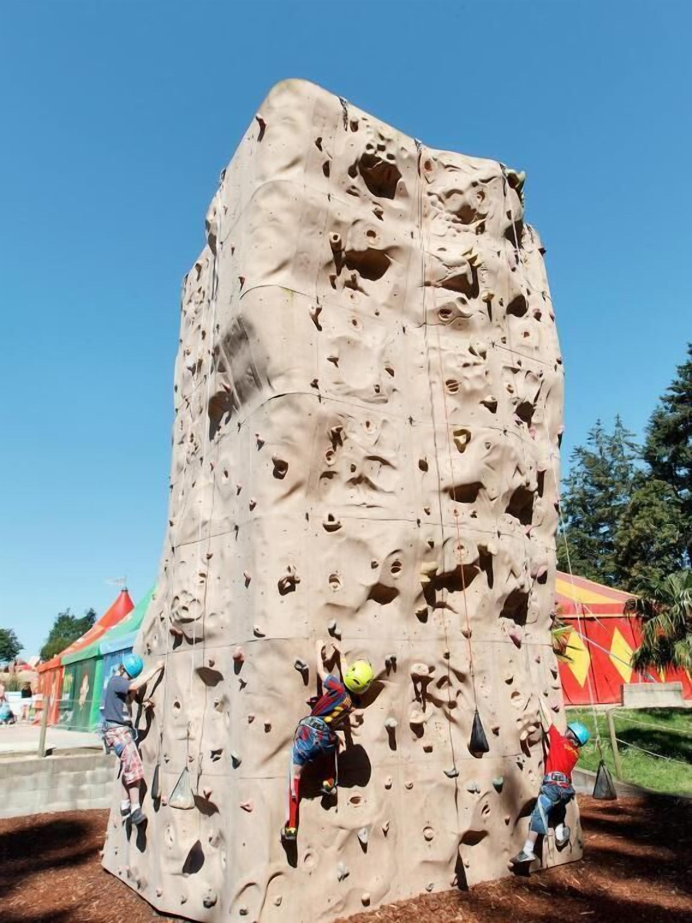 Un mur d’escalade avec plusieurs voies d’ascension et des grimpeurs.