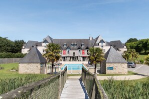 A large building with a swimming pool, stone walls, and a wooden deck leading to the pool. - Domaine Des Ormes (Epiniac)