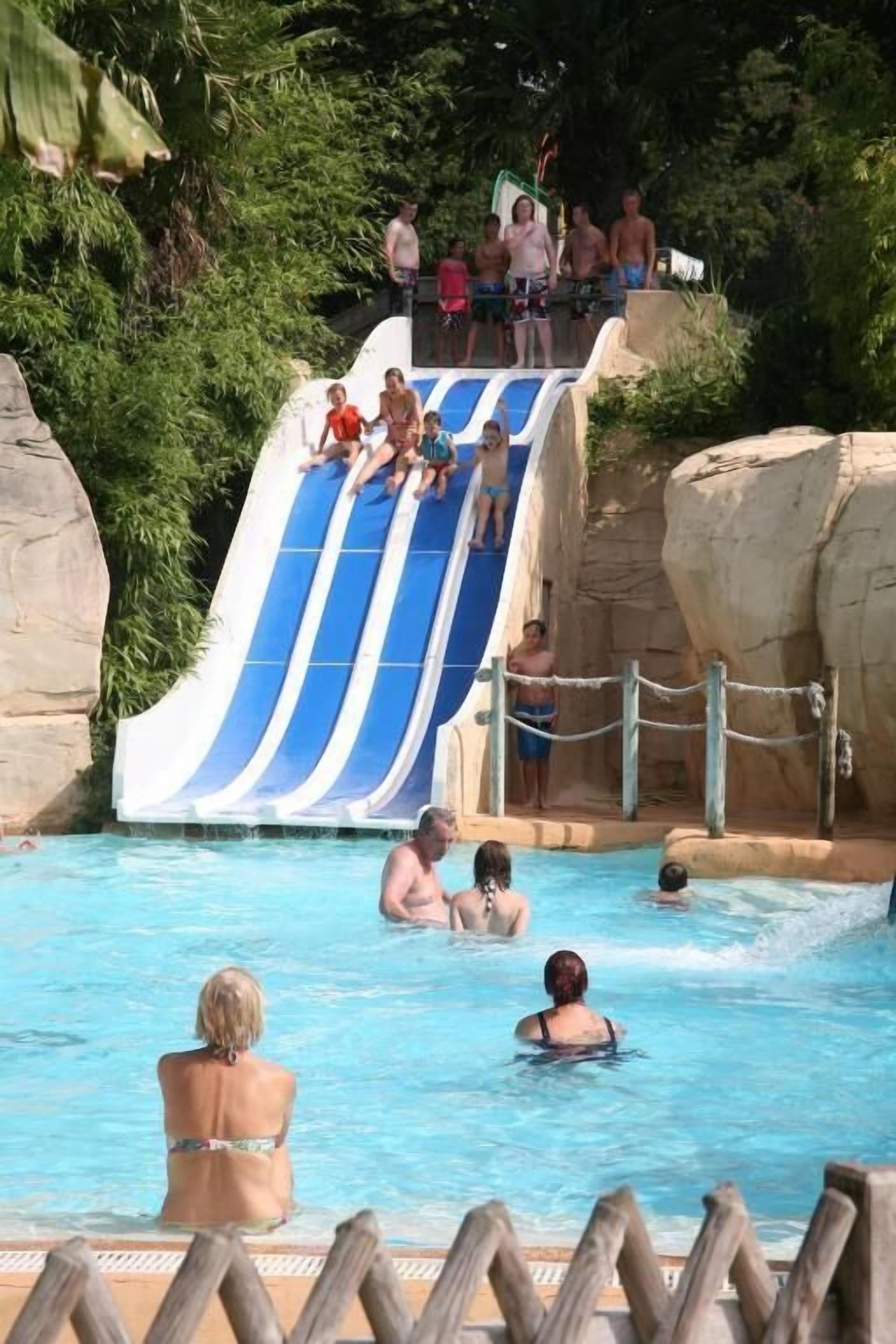 Zona de piscina amb tobogan d'aigua i persones nedant.