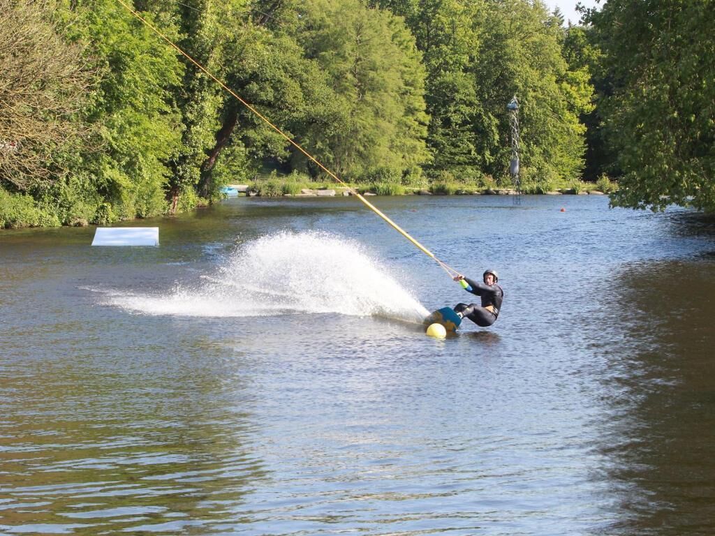 Une personne fait du wakeboard sur un lac entouré d’arbres.