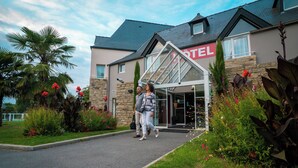 A hotel entrance with a stone facade, a glass entryway, and a well-maintained garden with various plants and flowers. - Domaine Des Ormes (Epiniac)