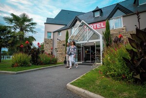 A hotel entrance with a stone facade, a glass entryway, and a well-maintained garden with various plants and flowers.
