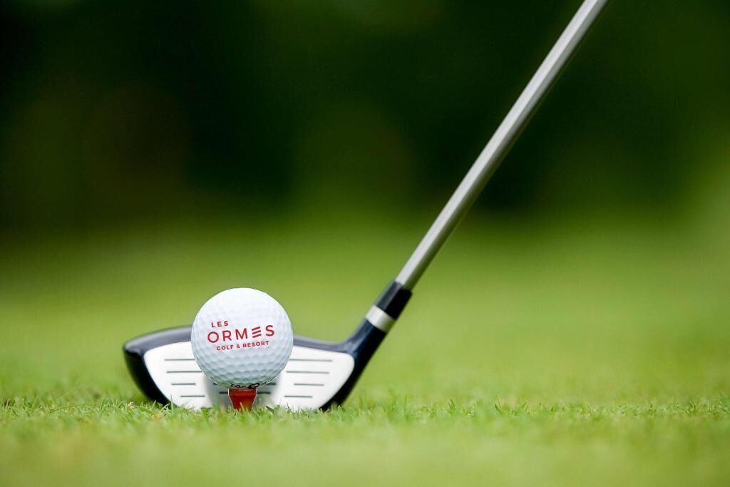 A golf ball on a tee with a golf club.