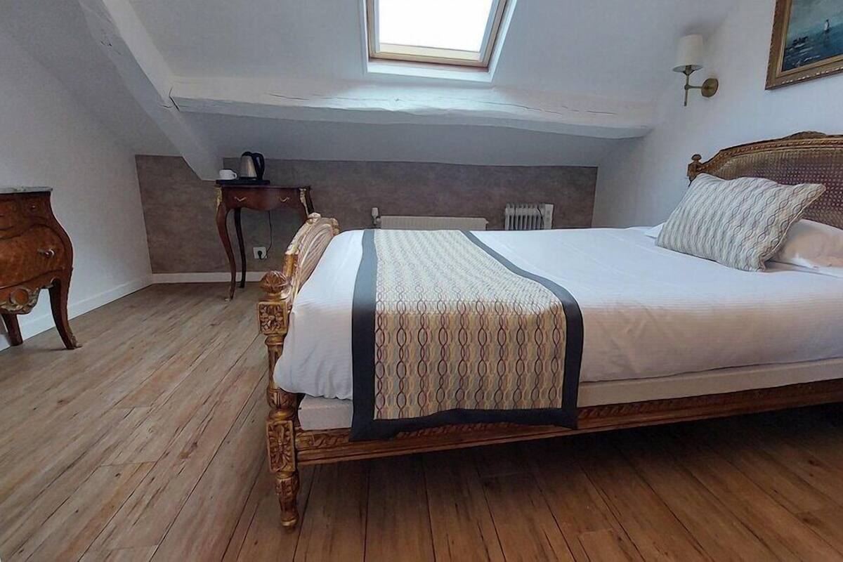 A bedroom with a wooden bed, a small bedside table, a radiator, and a skylight.