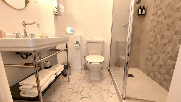 Un baño con suelo de baldosas hexagonales, un inodoro, un lavabo con toallero y una zona de ducha.