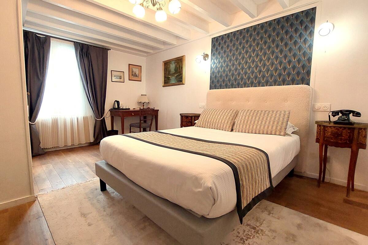 A bedroom with a bed, bedside tables, a desk, a chair, and a window with curtains.