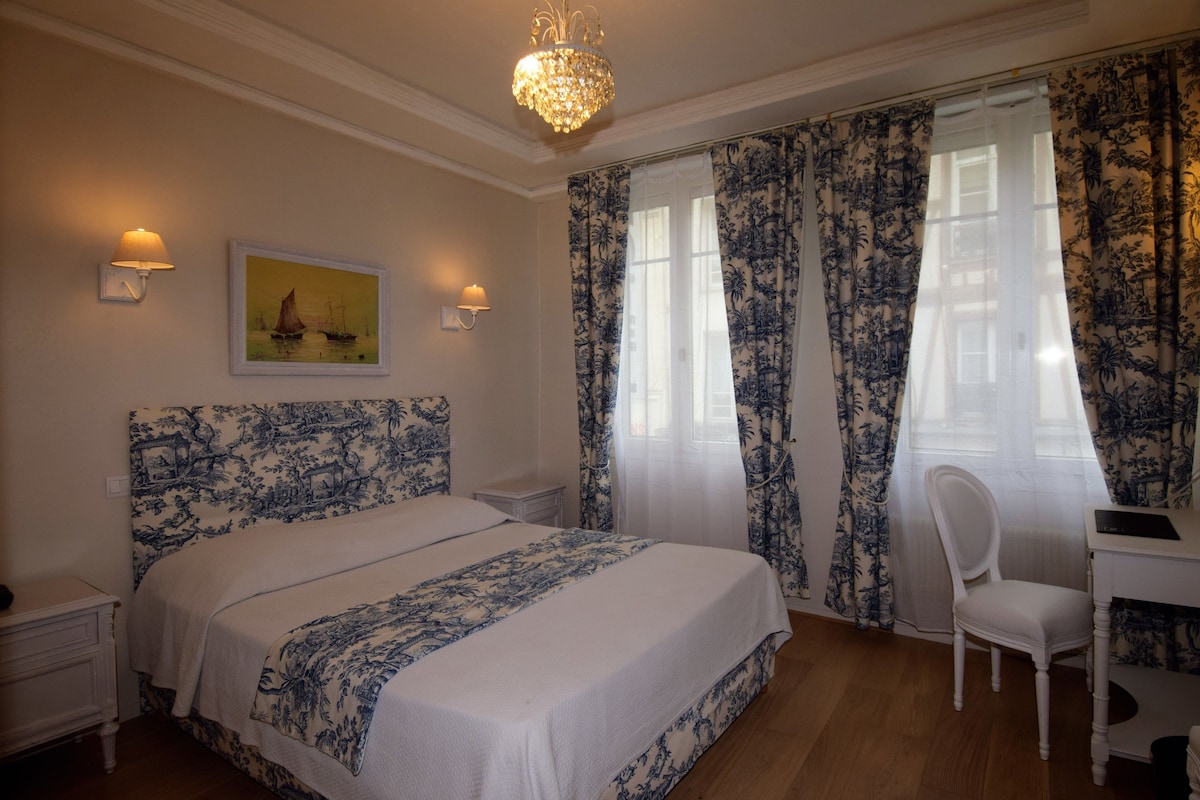 A bedroom with a bed, a desk, a chair, a chandelier, and curtains.