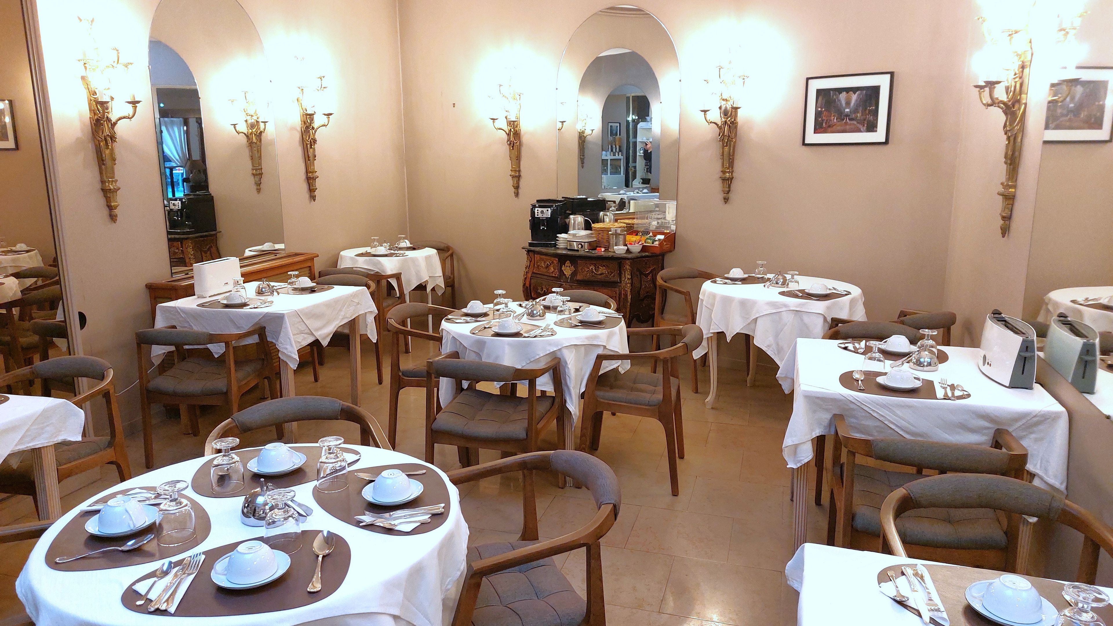 A dining area with round tables set for four, each with white tablecloths, silverware, and blue plates.