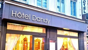 Um hotel chamado 'Hôtel Dandy', com grandes janelas e uma placa sobre a entrada.