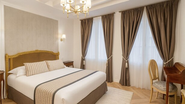 Quarto de hotel com uma cama grande, uma escrivaninha, uma cadeira e um candelabro.