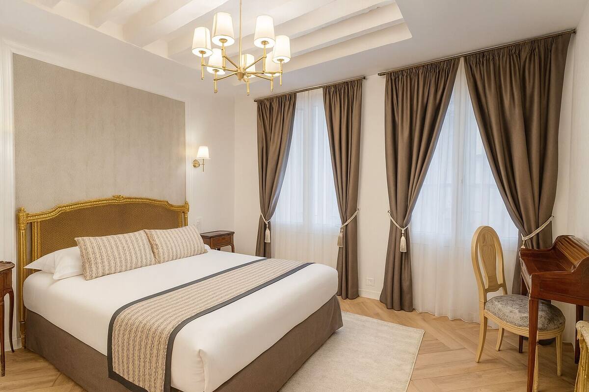 A hotel room with a large bed, a desk, a chair, and a chandelier.