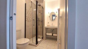 Casa de banho com sanita, chuveiro com divisória de vidro e lavatório com espelho.