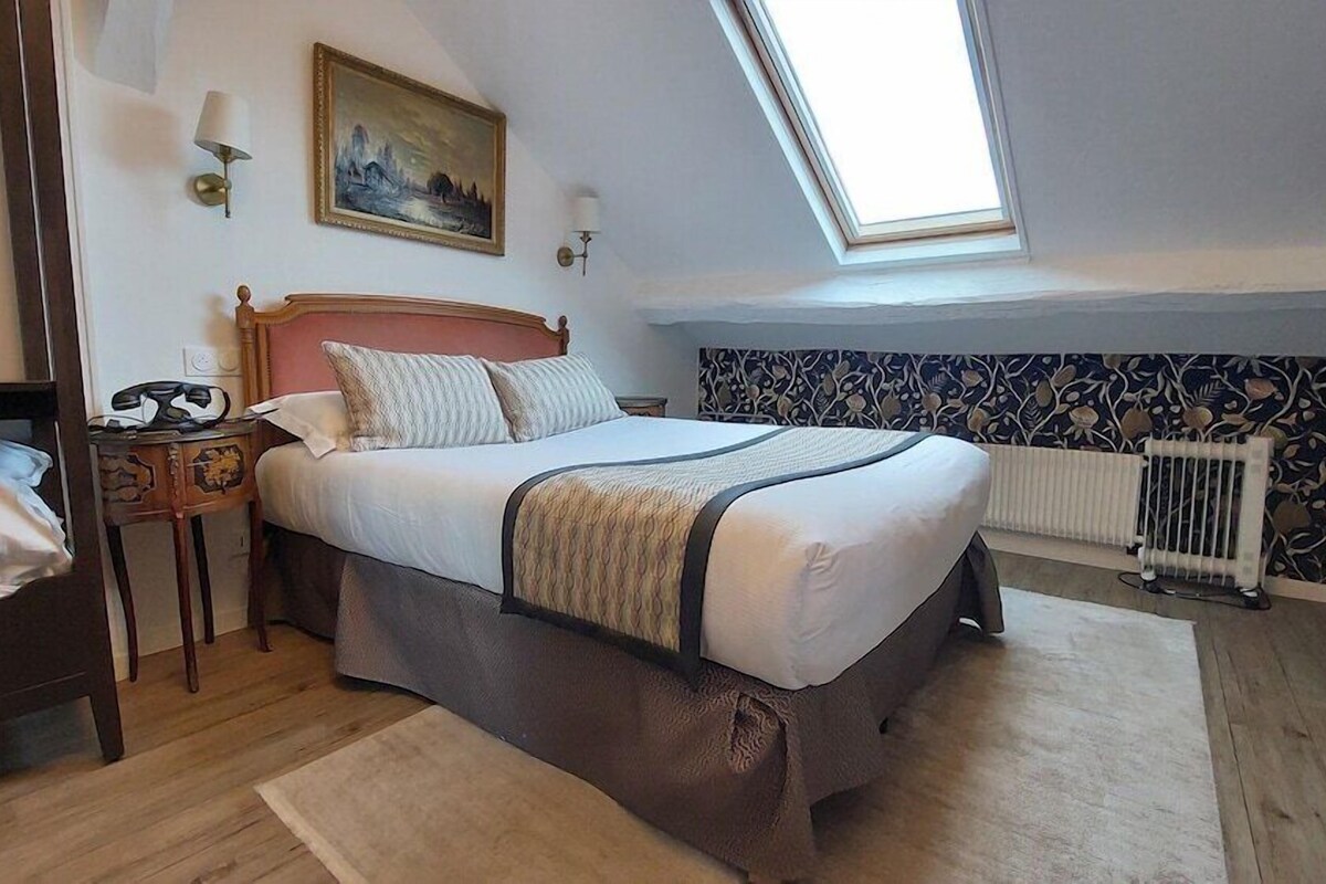 A bedroom with a bed, bedside tables, a radiator, a window, and a painting on the wall.