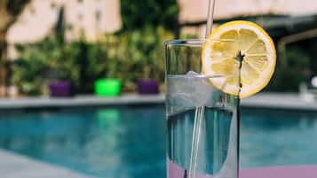 A glass of water with a lemon slice and straw by a poolside table with a purple cushion.