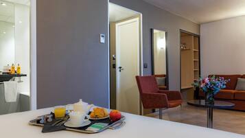A modern hotel room with a breakfast tray, a red armchair, and a sofa in the living area.