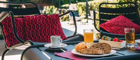 A dining table with breakfast items, including toast, fruit, and a beverage, set in an outdoor patio area with chairs and cushions.