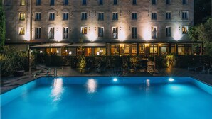 A hotel with a swimming pool, outdoor seating, and a well-lit facade.