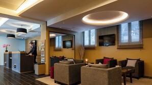 A modern lobby with a reception desk, seating area with sofas, and a TV mounted on the wall.