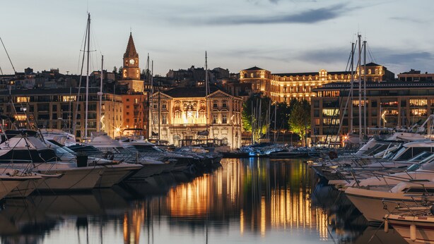 A marina with boats docked, a clock tower, and illuminated buildings. - Escale Oceania Marseille Vieux Port (Marseille)