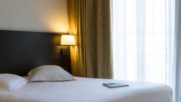 Una cama bien hecha con sábanas y almohadas blancas, una lámpara de noche y un libro sobre la cama.