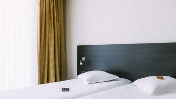 A hotel room with two beds, a dark headboard, a white wall, and a window with curtains.