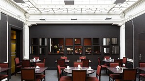 A hotel dining area with multiple tables and chairs, a dark wall with mirrors, and a high ceiling with ornate details. - Escale Oceania Marseille Vieux Port (Marseille)