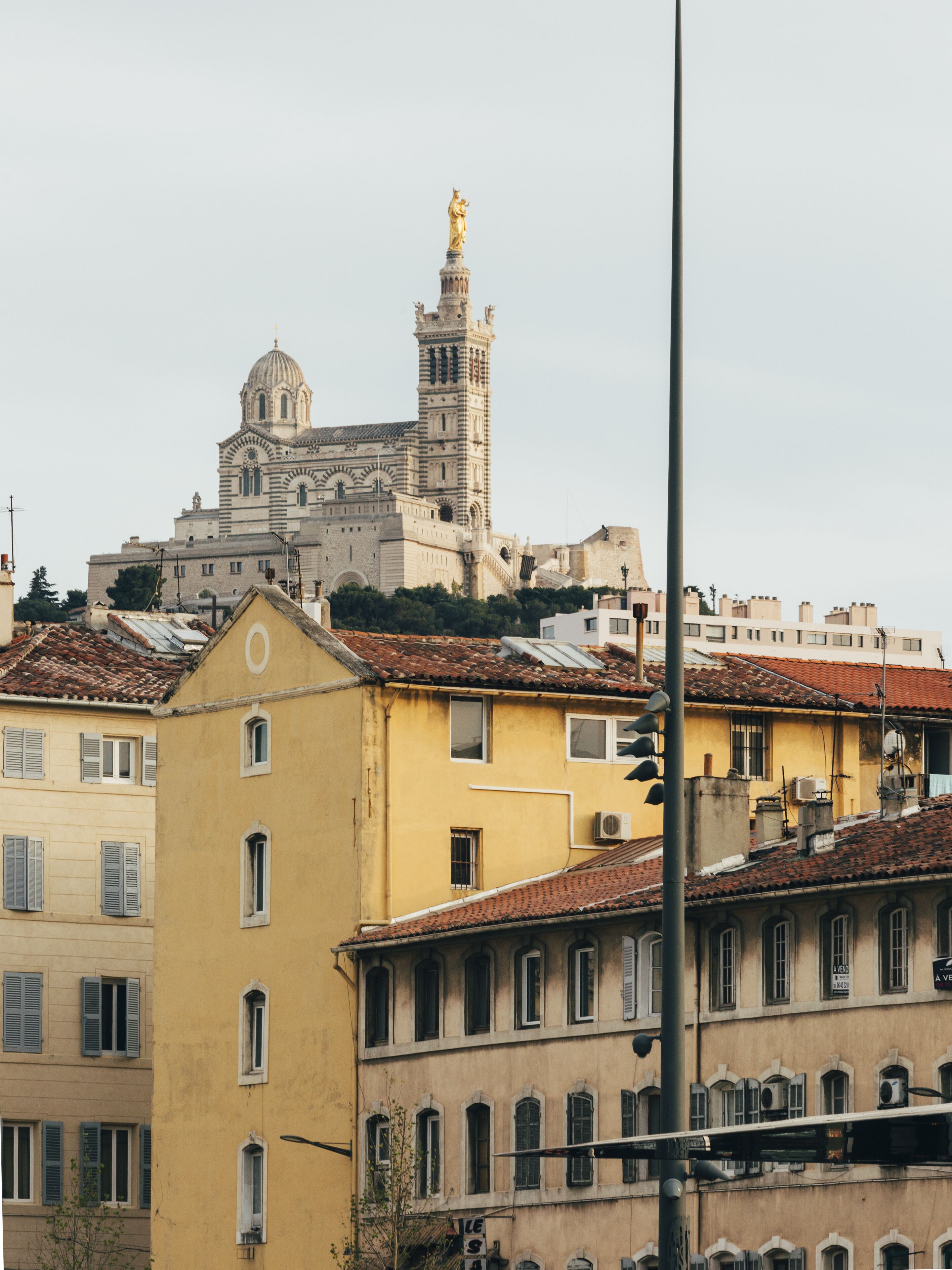 Un bâtiment historique doté d’une tour et d’un dôme imposants, entouré d’immeubles d’habitation aux toits recouverts de tuiles rouges et à l’architecture traditionnelle.
