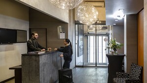 A reception desk with a man and a woman shaking hands, a black bag on the floor, and a patterned chair to the right. - Escale Oceania Marseille Vieux Port (Marseille)