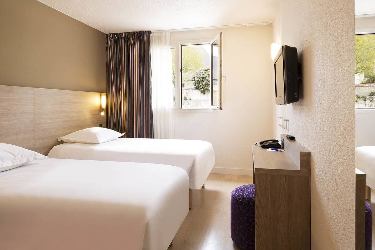 A hotel room with two beds, a small desk with a telephone, and a TV mounted on the wall.