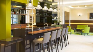 Zona de bar moderna con una barra alargada, varios taburetes y lámparas colgantes.