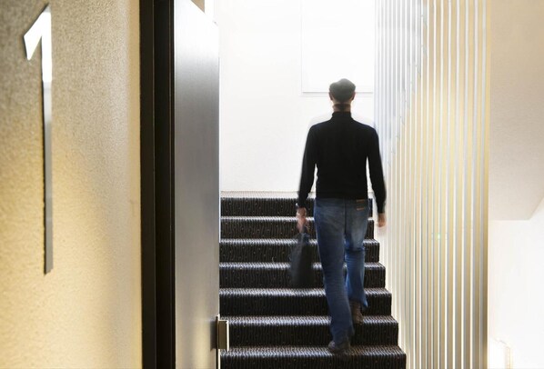 Una persona bajando una escalera con barandilla y un marco de puerta con un cartel de número.
