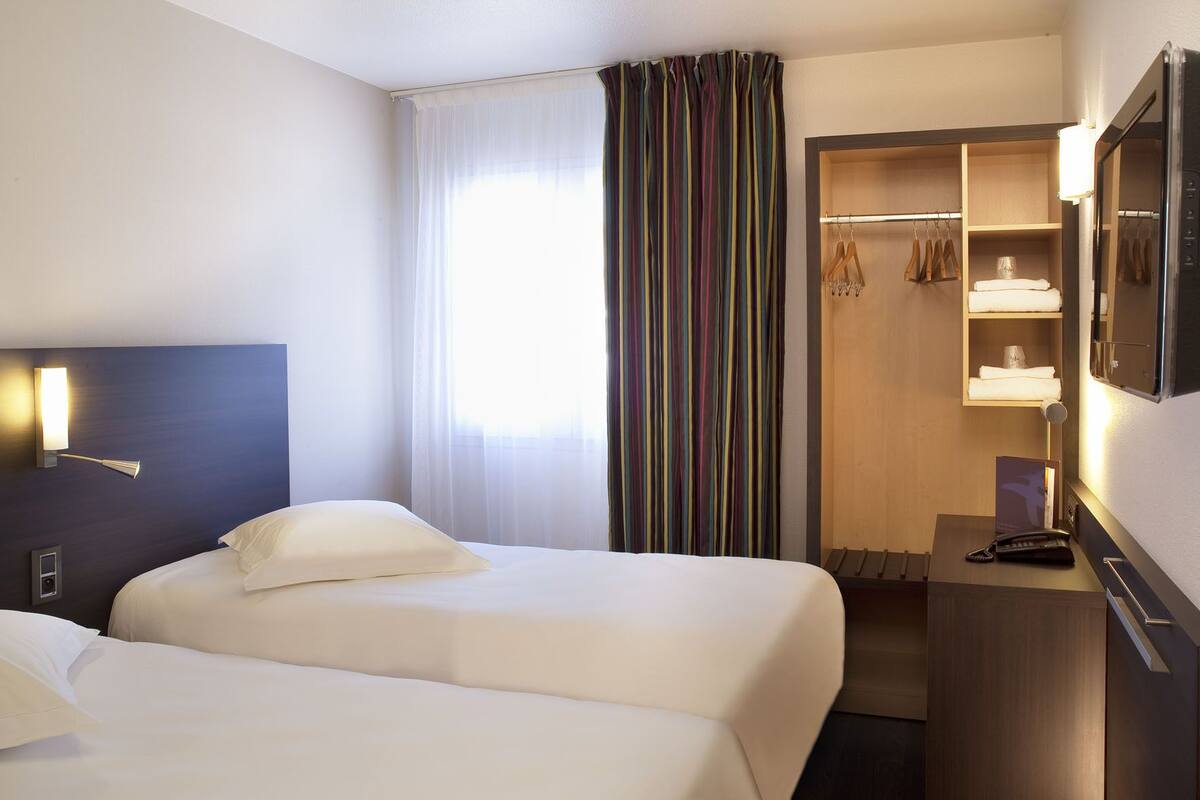 A hotel room with two beds, a walk-in closet, a desk with a phone, and a mirror.