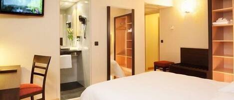 A hotel room with a bed, a TV, a desk, a chair, a mirror, and a wardrobe.