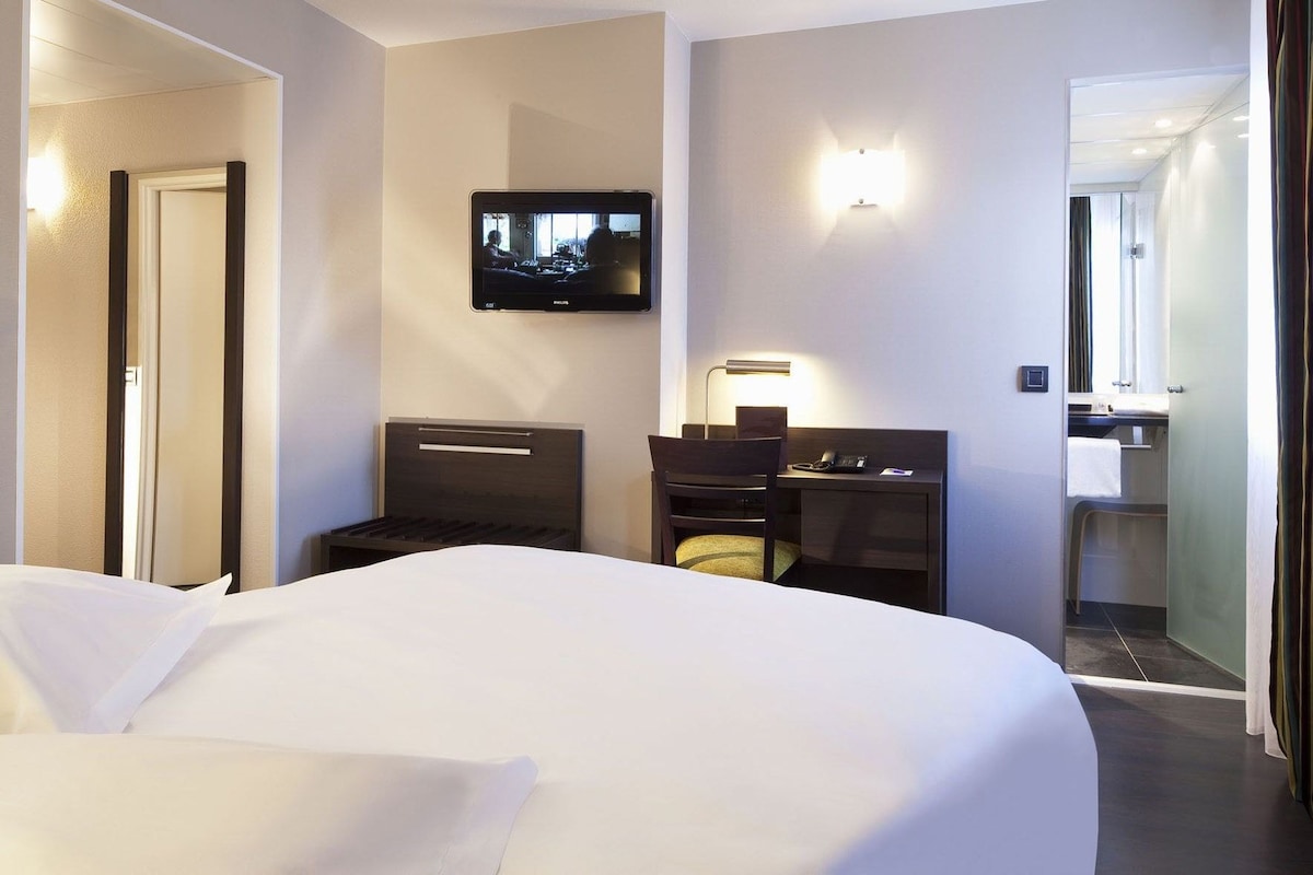 A hotel room with a large bed, a desk with a chair, a television mounted on the wall, and a mirror.