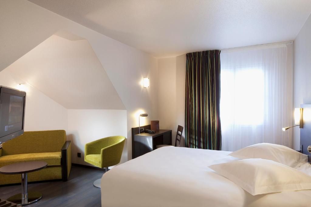 Une chambre d’hôtel avec un lit, un bureau, une chaise, une télévision et une fenêtre avec des rideaux.