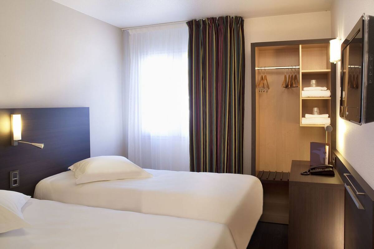 A hotel room with two beds, a wardrobe, a desk with a phone, and a mirror.