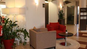 A lobby with a beige sofa, a red armchair, a small round table, and potted plants. - Escale Oceania Vannes (Vannes)
